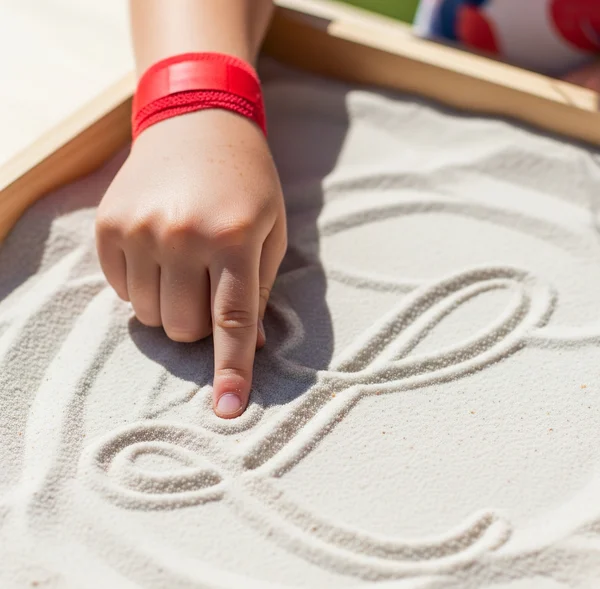Childs hand tracing cursive letter in sand sensory tray