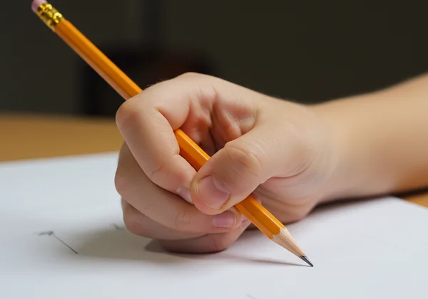 A close-up of a child's hand using a tripod pencil grip.